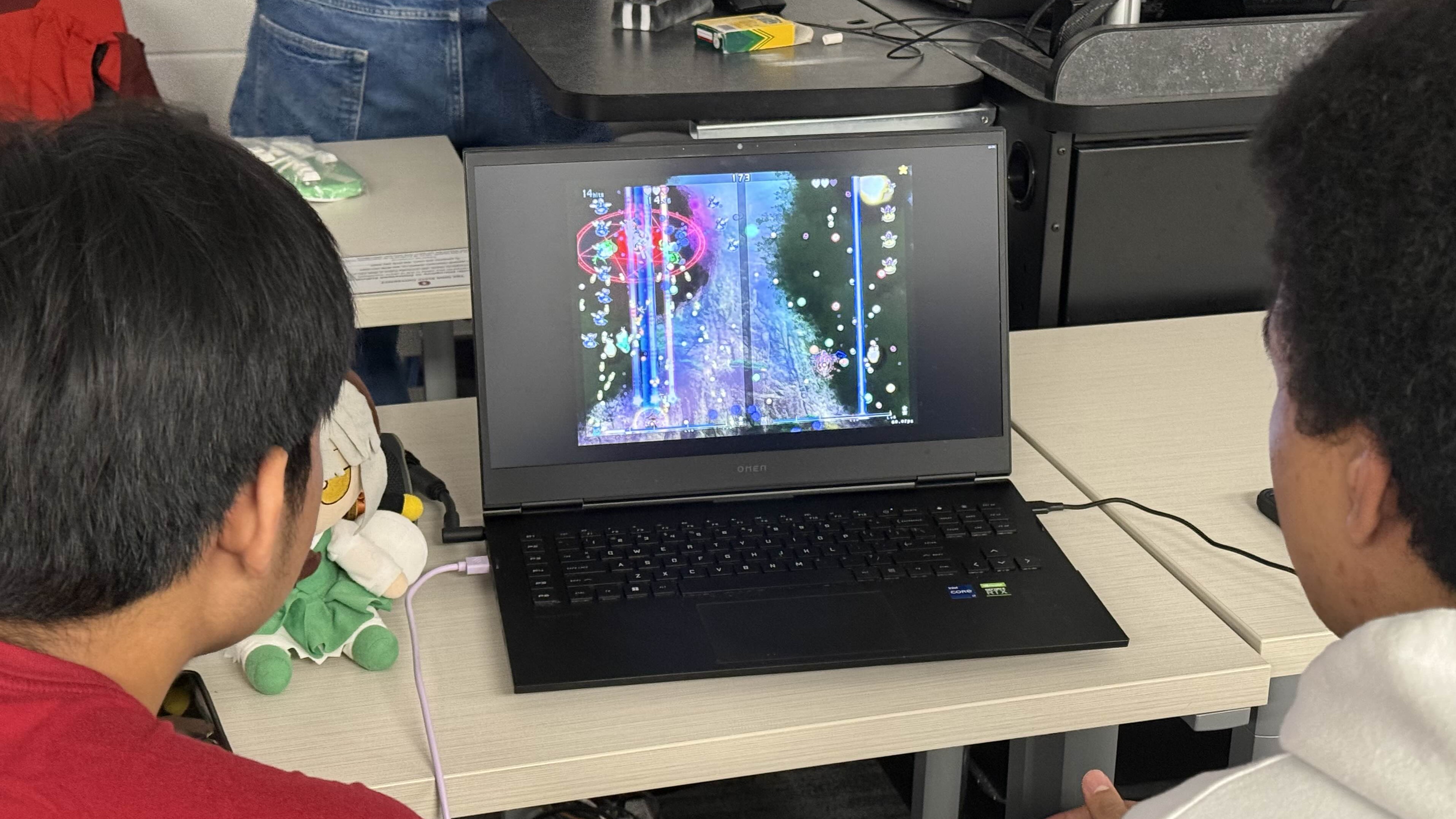 Two people sitting in front of a computer playing Phantasmagoria of Flower View.
